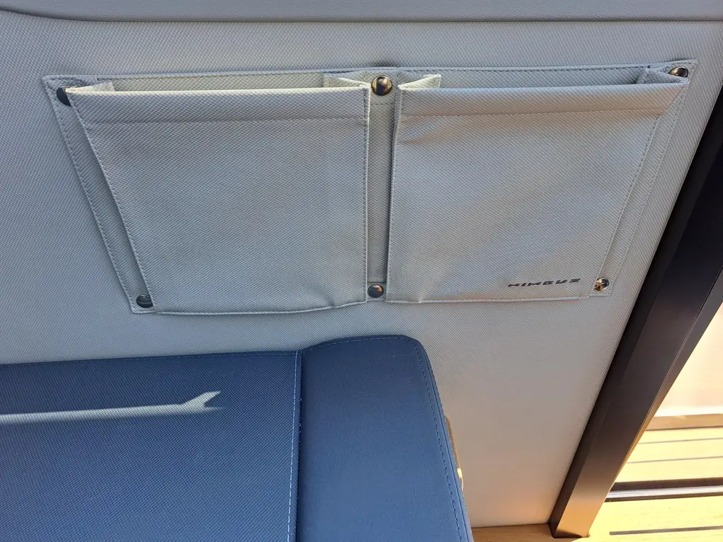 Twin grey storage pockets on an aircraft seatback, featuring the logo "NINEVS" and a blue seat cushion below.